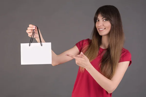 Una chica con una camiseta roja con una bolsa de regalo blanca. Mujer ofrece comprar un producto . —  Fotos de Stock