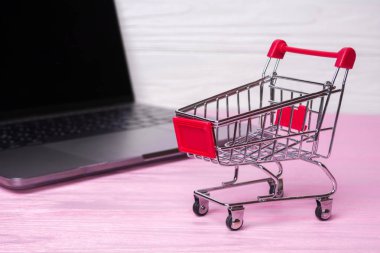 Boş alışveriş arabası ve pembe ahşap arka plan üzerinde bir dizüstü bilgisayar