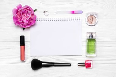 Kozmetik ve aksesuar şık düzeni. Tırnak cilası, yüzük, fırça, dudak parlatıcısı, parfüm, tırnak cilası, göz farı, Şakayık Çiçeği ve metni ahşap arka plan üzerinde beyaz Not defteri.