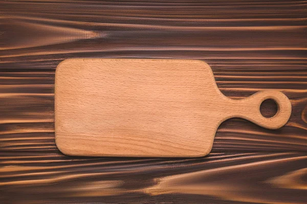 Kitchen cutting board on a wooden background, top view — Stock Photo, Image