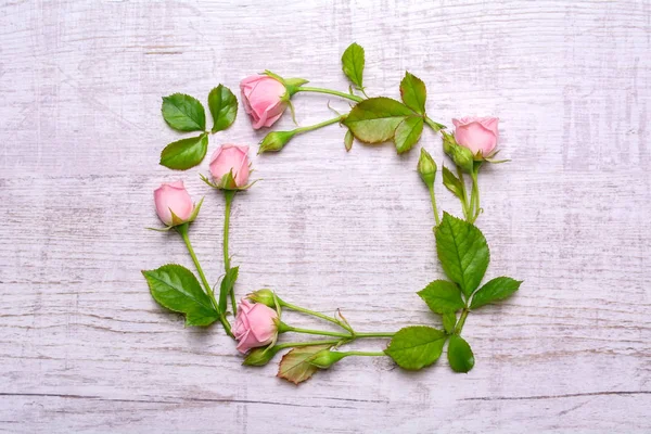 Round frame of delicate flowers. Pink roses on a wooden background
