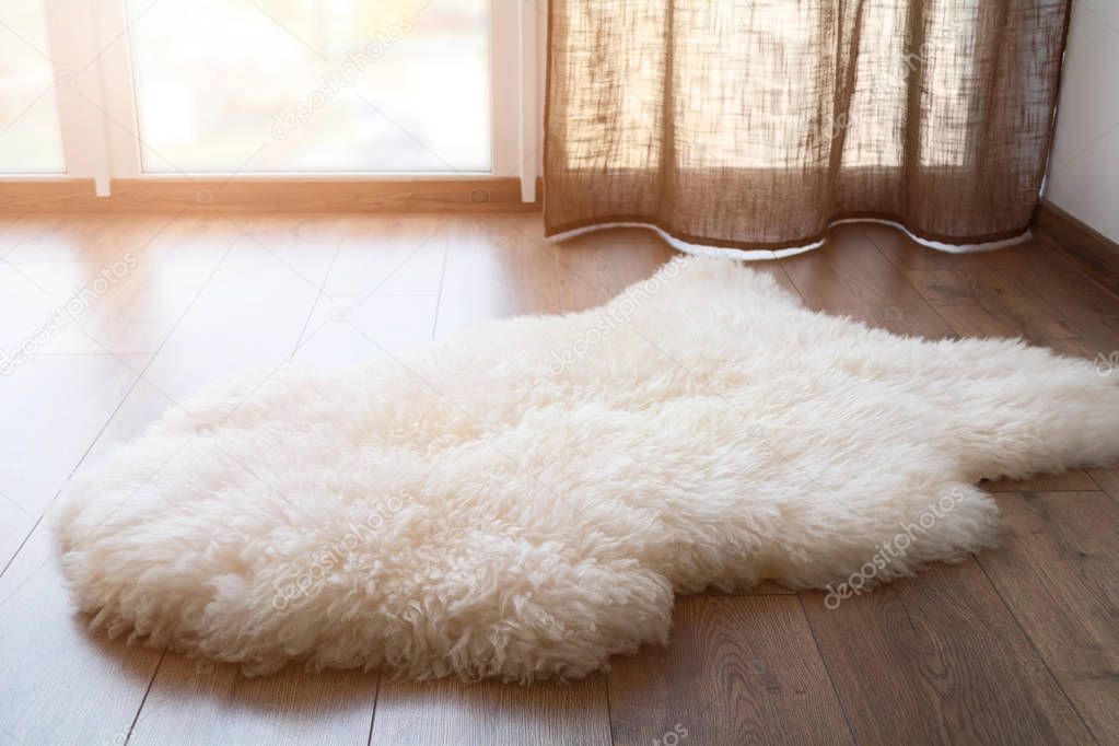 Sheep skin on the laminate floor in the room. Cozy place near the window. Sunny day.