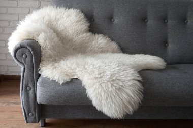 White sheep skin on a gray sofa. A cozy place to relax in the apartment. Modern Scandinavian style interior clipart