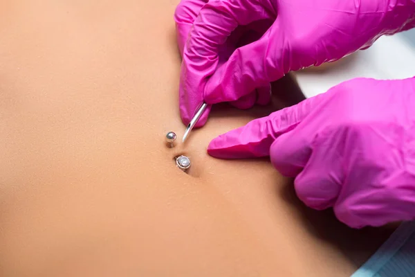 Belly button piercing. The beautician does the piercing procedure