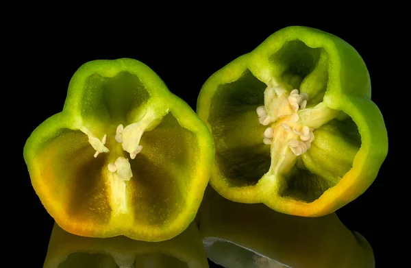 A Green Bell Pepper, cut in half, isolated on black reflective background.