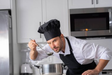 Profesyonel üniformalı modern şef. Kaşıkla tencereye çorba karıştıran erkek aşçının eline yakın plan. Yemek pişirme, aşçılık ve insan konsepti - erkek aşçı tencereli veya tencereli.