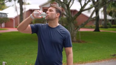 Sporcu koşudan sonra susuzluğunu suyla giderir. Islak tişörtlü sporcu yoğun fitness aktivitesi sırasında susuz kalıyor. Sağlıklı yaşam tarzı ve fiziksel iyileşme kavramı.