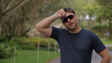 Profesyonel atlet yoğun koşudan sonra ter silmek için durur. Açık hava maratonu sırasında güneş gözlüğü takan sporcu yorgun görünüyor. Dayanıklılık, sıcaklık ve spor yorgunluğu kavramı.