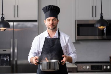 Profesyonel üniformalı modern şef. Kaşıkla tencereye çorba karıştıran erkek aşçının eline yakın plan. Yemek pişirme, aşçılık ve insan konsepti - erkek aşçı tencereli veya tencereli.