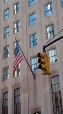 New York 'ta Beşinci Cadde' de Amerikan bayrağı taşıyan tarihi binanın önünde trafik ışıkları asılı. Kent sahnesi şehir hayatını, yaya hareketini, turizmi ve ABD 'nin ikonik sembolünü yakalıyor.