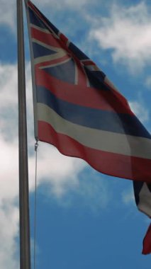Hawaii 'nin ulusal bayrağı bulutlu mavi gökyüzüne karşı uzun bir direkte dalgalanıyor. Sembol tarihi, kültürü ve kimliği temsil eder. Sahne, Pasifik bölgesindeki vatanseverlik, seyahat ve devlet gururunu yansıtıyor..