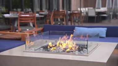 Yanan alevlerle dolu modern açık hava terası rahat bir salon ortamı yaratıyor. Rahat koltuklar, sonbahar havası ve ılık ışık, şehir yaşam tarzında rahatlama, konukseverlik ve pozitif ruh halini vurguluyor