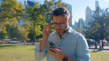 İş adamı Central Park 'ta dururken akıllı telefon kullanır. Gündelik tişörtlü turist cep telefonundaki mesajları ve uygulamaları kontrol ediyor. Sahne, New York 'ta yaşam tarzı, teknoloji ve modern iletişimi yansıtıyor.