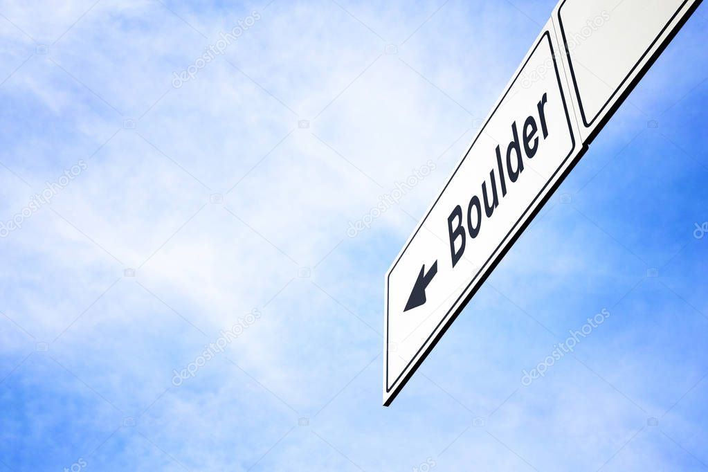 White signboard with an arrow pointing left towards Boulder, Colorado, USA, against a hazy blue sky in a concept of travel, navigation and direction. Path included for the signboard
