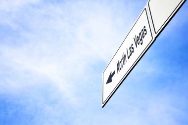 Bir ok işaret ile beyaz tabela North Las Vegas, Nevada, ABD doğru seyahat, gezinti ve yön kavramı puslu bir mavi gökyüzünde karşı yaptı. Tabela için yola