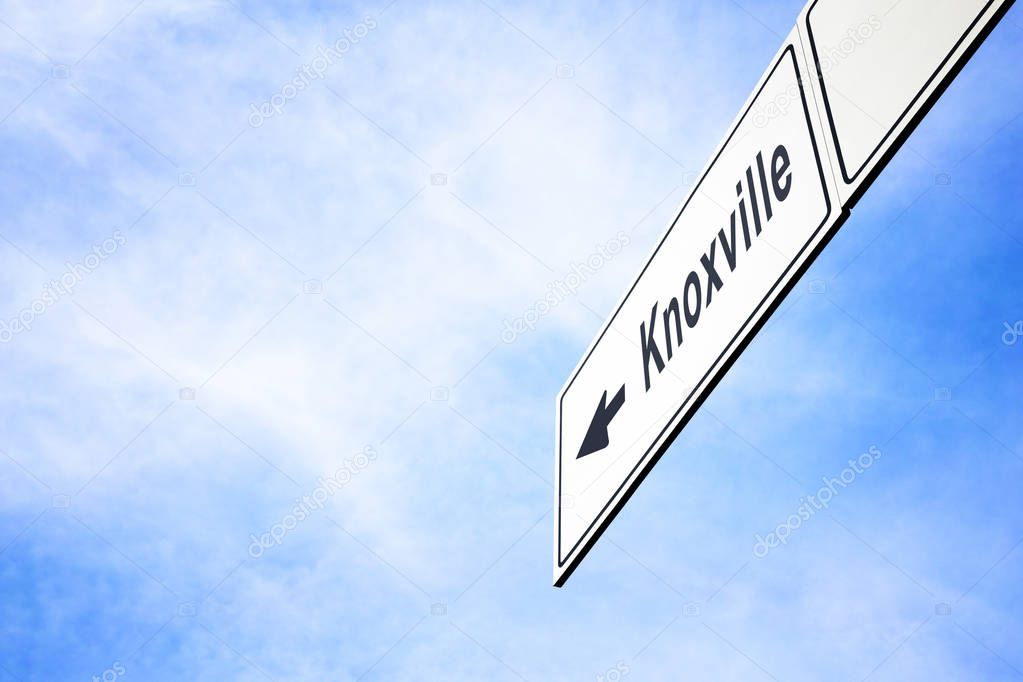 White signboard with an arrow pointing left towards Knoxville, Tennessee, USA, against a hazy blue sky in a concept of travel, navigation and direction. Path included for the signboard