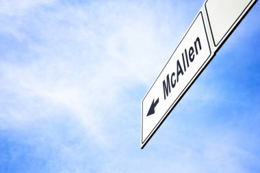 White signboard with an arrow pointing left towards McAllen, Texas, USA, against a hazy blue sky in a concept of travel, navigation and direction. Path included for the signboard clipart
