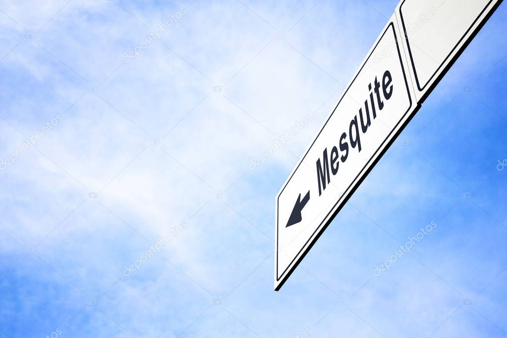 White signboard with an arrow pointing left towards Mesquite, Texas, USA, against a hazy blue sky in a concept of travel, navigation and direction. Path included for the signboard