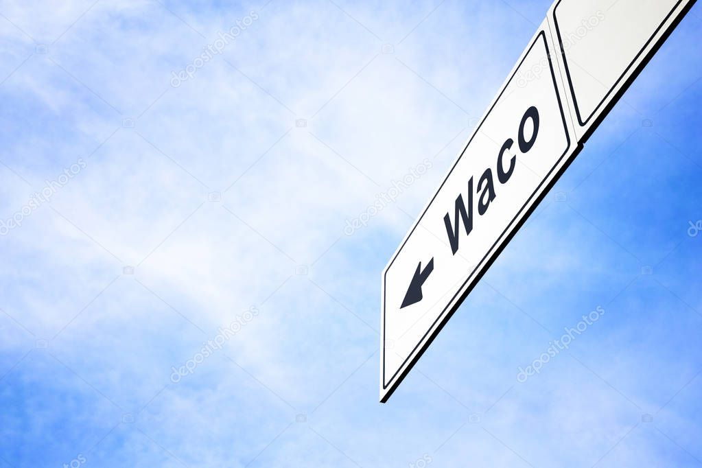 White signboard with an arrow pointing left towards Waco, Texas, USA, against a hazy blue sky in a concept of travel, navigation and direction. Path included for the signboard