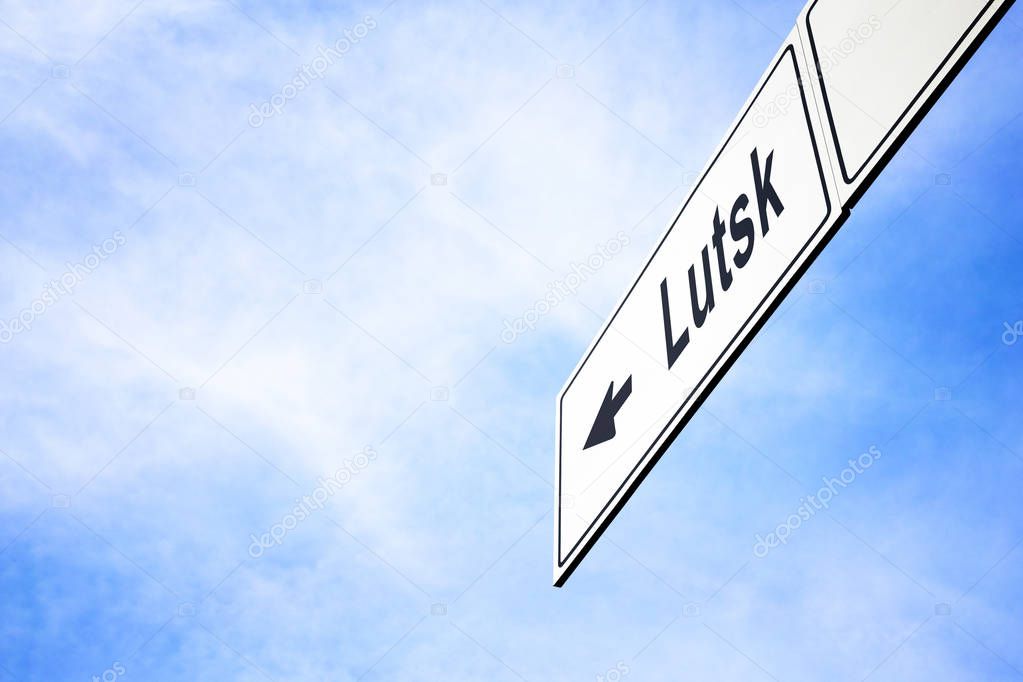 White signboard with an arrow pointing left towards Lutsk, Ukraine, against a hazy blue sky in a concept of travel, navigation and direction. Path included for the signboard