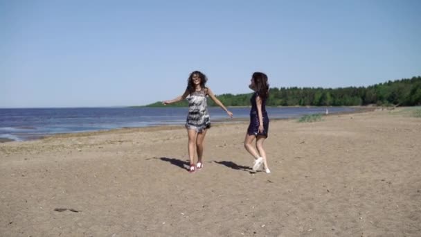 Две девушки бегают и танцуют на пляже в платьях — стоковое видео