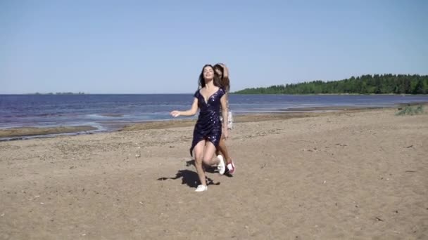 两个年轻女子在沙滩上穿着礼服奔跑跳舞 — 图库视频影像
