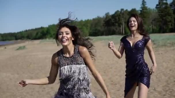 Twee jonge vrouw lopen en dansen op het strand in jurken — Stockvideo