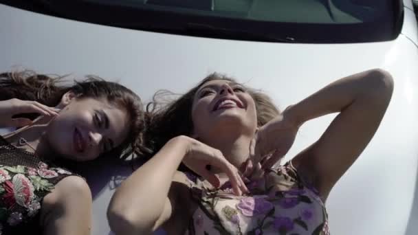Две девушки позируют на автомобильном капоте — стоковое видео