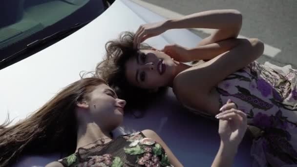 Две девушки позируют на автомобильном капоте — стоковое видео