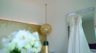Lüks Otel yatak odasında bir ayna üzerinde gelinlik. Beyaz güllerden gelin buketi.