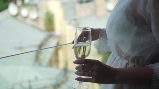 Mujer joven en el balcón o terraza en lencería blanca sujetador y albornoz beber champán de cristal. Vista de la ciudad en segundo plano — Vídeo de stock