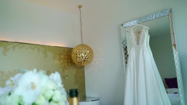 Trouwjurk op een spiegel in de slaapkamer in luxehotel. Bruids boeket van witte rozen. — Stockvideo