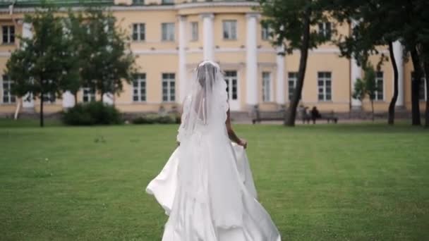 Jeune mariée courant dans un parc au ralenti ondulant robe à la journée nuageuse — Video