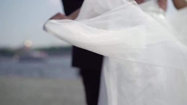 Жених и невеста обнимаются на городской набережной, невеста размахивает вуалью медленно — стоковое видео