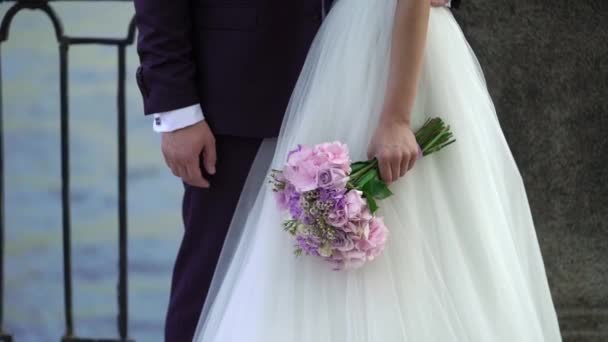 Bride and groom embracing in a city embankment, bride with bouquet — Stock Video