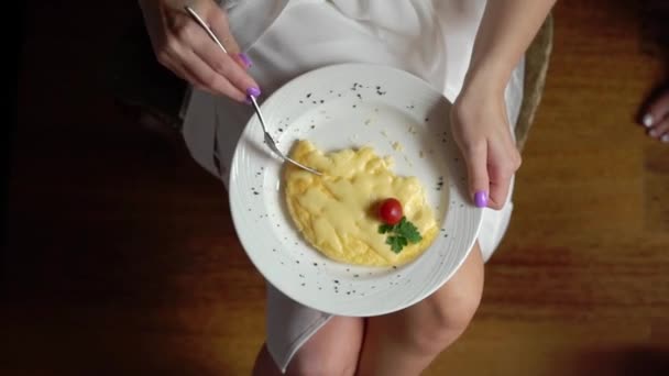 Topputsikt over kvinnelige hender som kutter stekt egg med kniv og gaffel. Nær ved å spise stekte egg. Tradisjonelle frokostegg i hvit tallerken – stockvideo