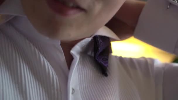 Un uomo in giacca e cravatta, una camicia bianca, tiene in mano un papillon viola o blu. Un uomo d'affari mette su un bowtiek per il suo matrimonio — Video Stock