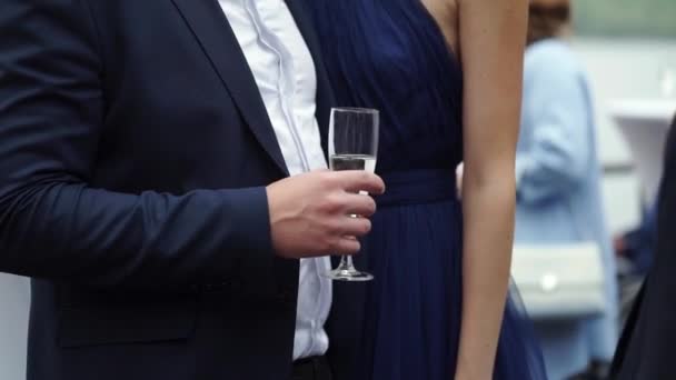 Fiatal ember tartja egy pohár pezsgővel, átölelve nő kék ruhában szabadban a partin — Stock videók