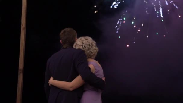 結婚式の日に夜の空で爆発する花火を見て美しいスタイリッシュな新婚のカップル — ストック動画
