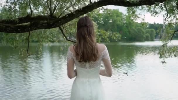 La mariée avec un bouquet à la main se tient sur le fond d'une rivière. Vue arrière. Rubans sur bouquet agitant du vent .