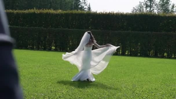 Молода наречена в розкішній весільній сукні з махаючою літаючою тканиною, модна жінка позує в парку. Біжить від нареченого і кружляє — стокове відео