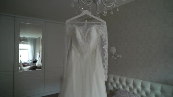 Luxury wedding dress hanging in bedroom. Silhouette of amazing brides lace gown in light. Morning preparation, getting ready — Stock Video