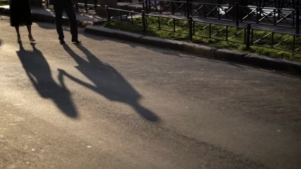 Hombre y mujer joven caminando por una calle. Pareja cogida de la mano en su cita en una calle de la ciudad por la mañana temprano, sombras en el suelo — Vídeos de Stock