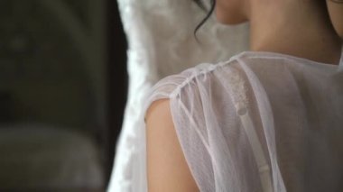 Dikiz gelini düğünden önce sabahları iç çamaşırı. Beyaz sabahlık gelinin düğün töreni için hazırlanıyor. Beyaz elbisesini tutan kız