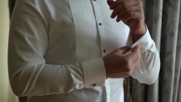 Бизнесмен носит запонку, мужчина кладет и регулирует запонку на белой рубашке, жених готовится утром перед свадьбой — стоковое видео
