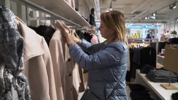 Wanita muda cantik memilih pakaian di toko — Stok Video