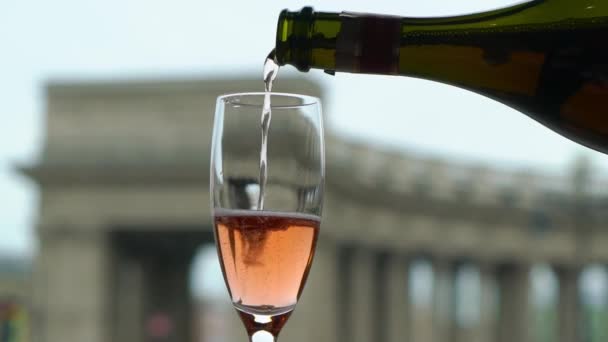 Versare champagne rosa o spumante a bicchiere dalla bottiglia. Città europea sullo sfondo . — Video Stock