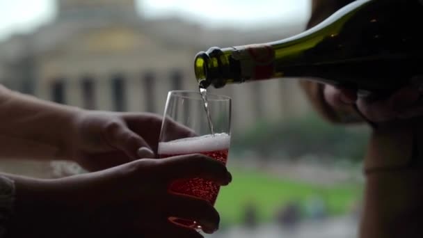 Наливать розовое шампанское или игристое вино в бокал из бутылки. Европейский город на заднем плане . — стоковое видео