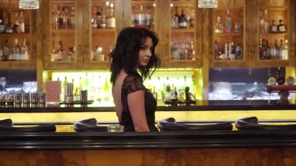 Молодая сексуальная брюнетка в черном вечернем платье в ресторане или баре — стоковое видео