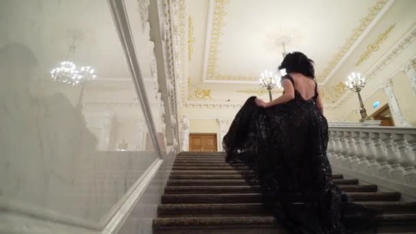 若い宮殿や高級ホテルの大理石の石のはしごで 階に行く黒のイブニング ドレスでセクシーなブルネットの女性 実行して落ちる — ストック動画